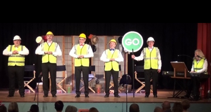5 men and 1 woman in hi-vis jackets holding a green 